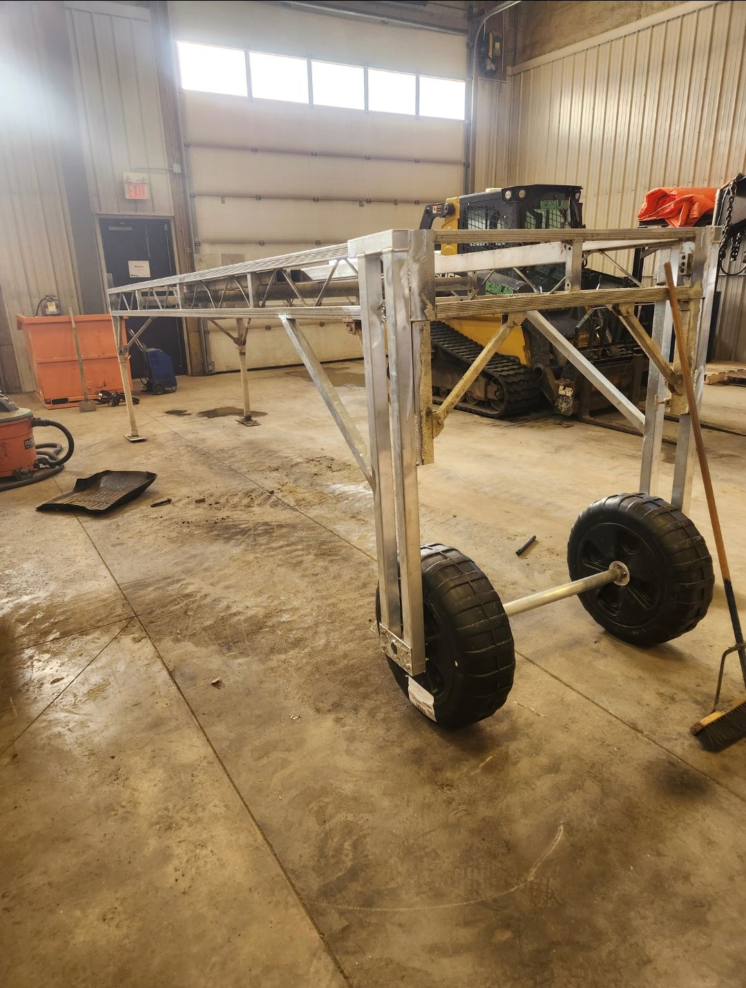 Metal cart frame with large wheels in a workshop/garage, near tools and equipment on a concrete floor.