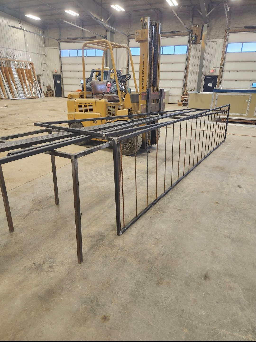 Industrial workshop with a large black metal frame on the floor and a yellow forklift in the background.
