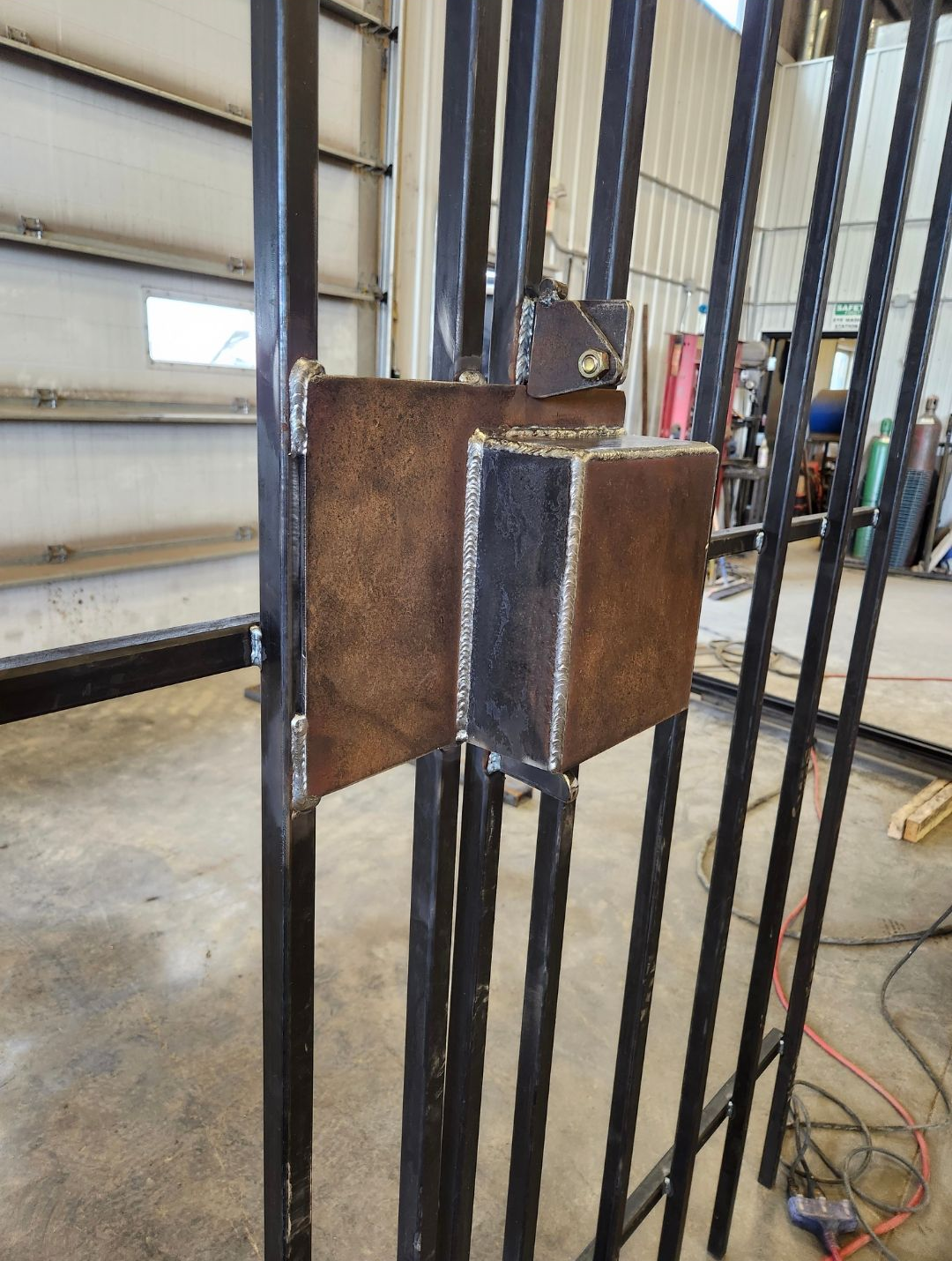 Close-up of a welded metal bracket on vertical steel bars in a workshop.