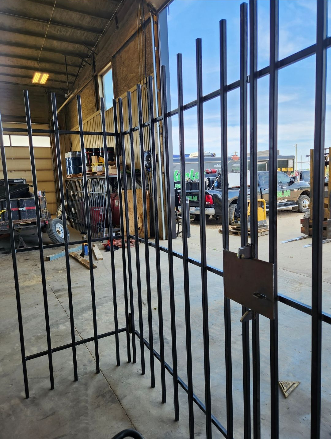 Metal security gate inside an open garage, looking out onto a parking lot on a sunny day