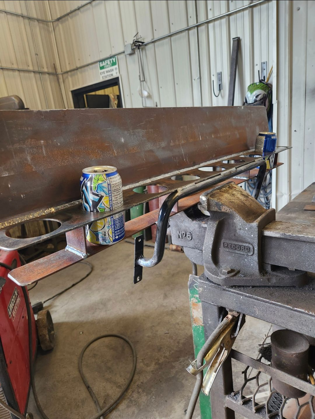 Metal pipe clamped in a workshop vise, with a spray can and tools on a workbench.