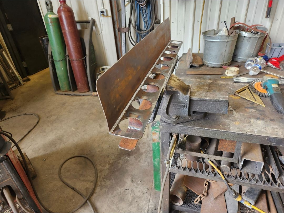 Rusty metal plow blade and workshop tools in a cluttered garage with a workbench.