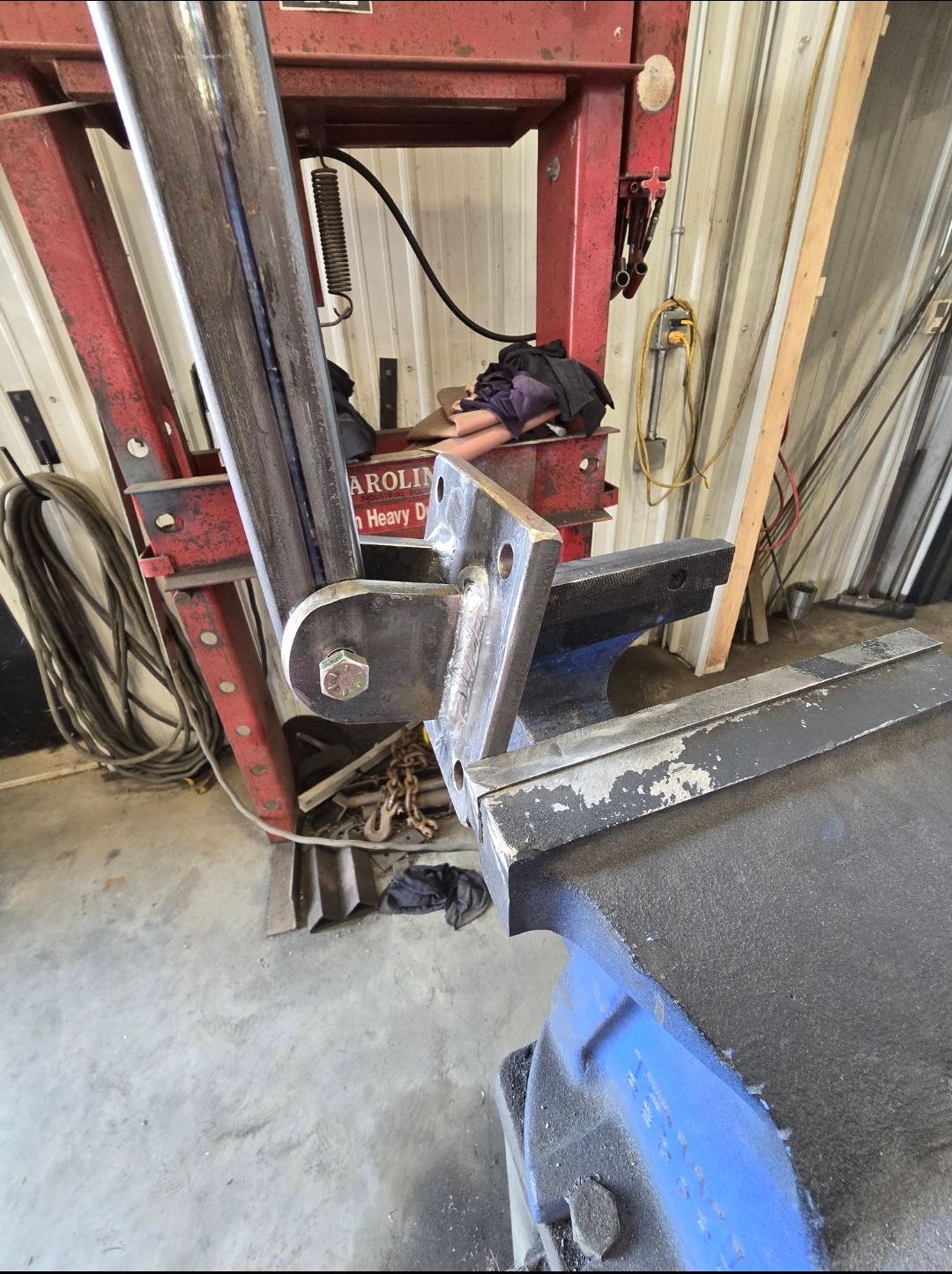 Metal clamp attached to a red and beige workshop machine in a cluttered industrial setting