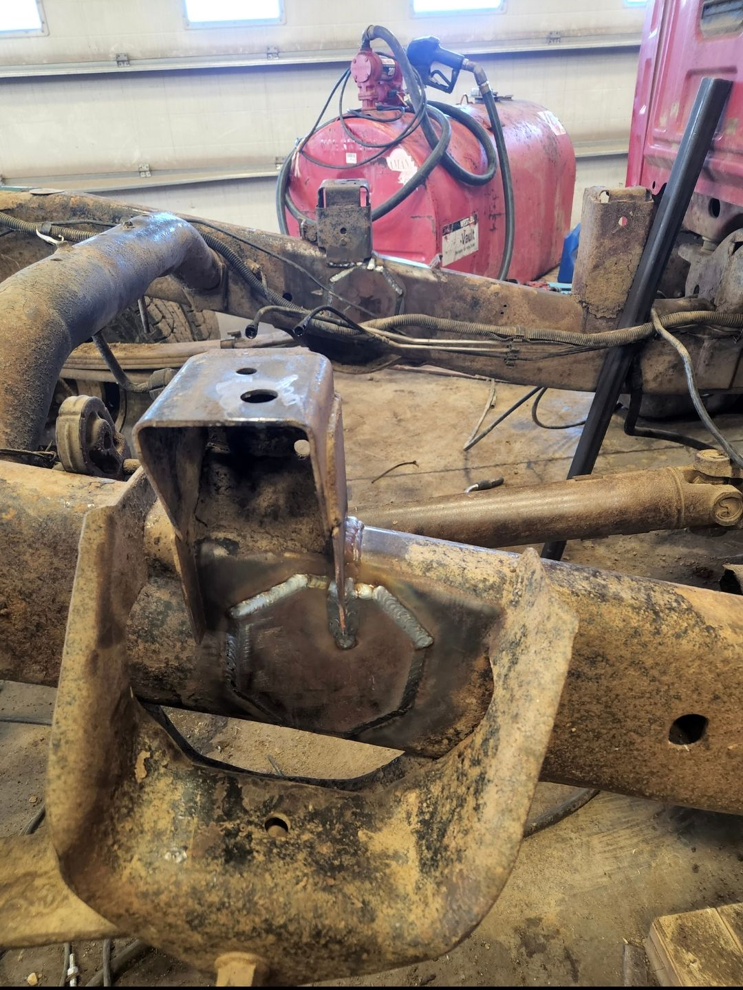 Close-up of muddy heavy machinery parts in a workshop, with hoses and a red tank in the background
