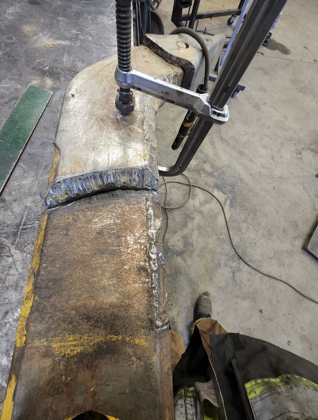 Weathered industrial pipe on concrete floor, with a metal clamp and cable attached.
