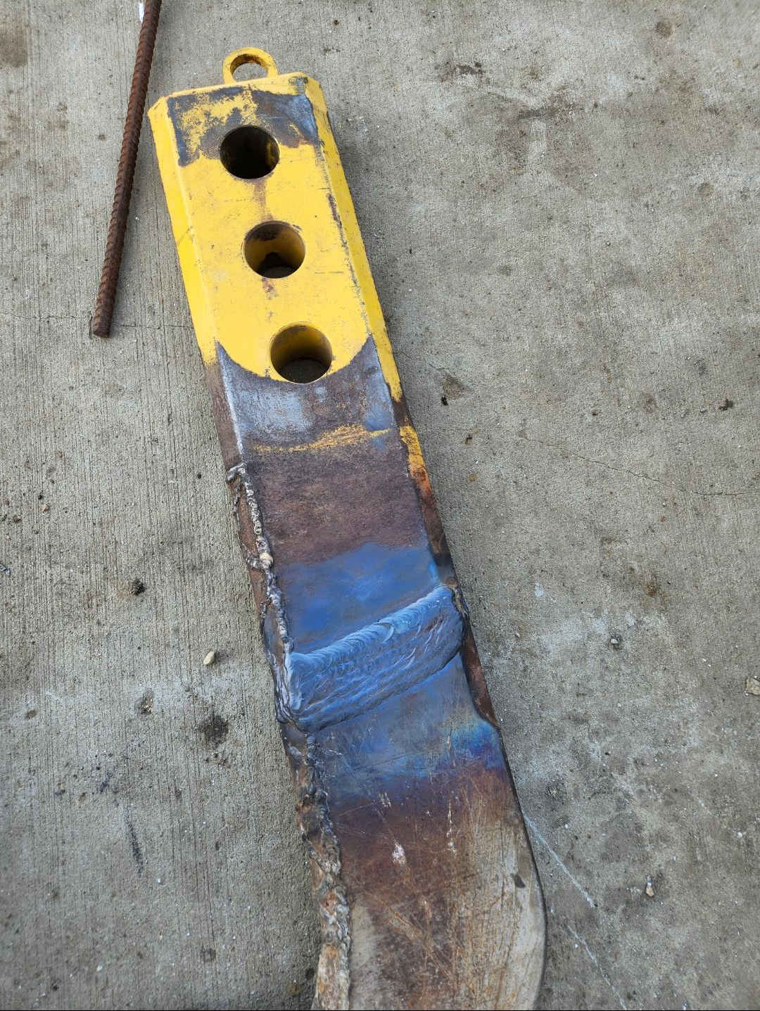 Yellow and rusted metal tool head with a curved, worn blade on a concrete surface
