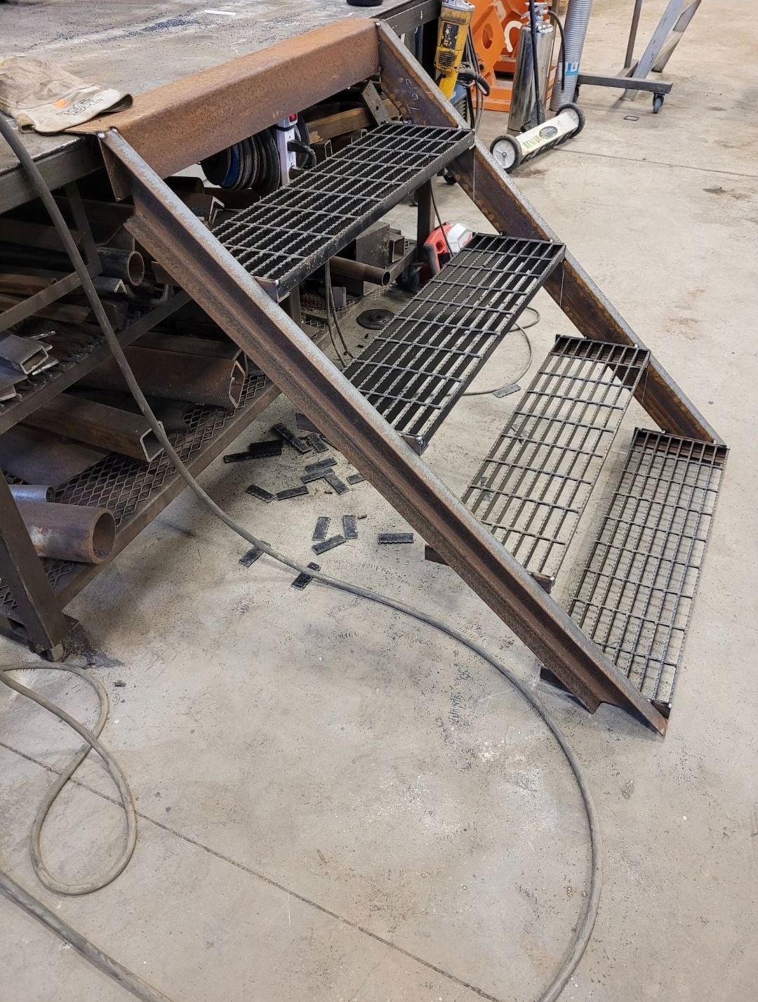 Metal staircase with grated steps beside a workbench in a workshop.
