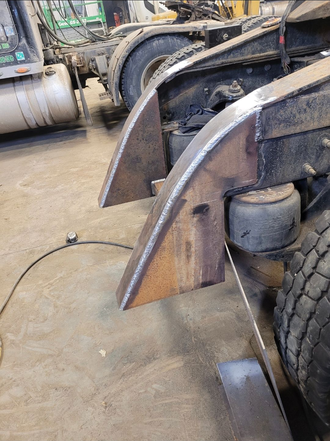 Close-up of a truck with two rusted metal forks or clamps on the front, in a workshop garage