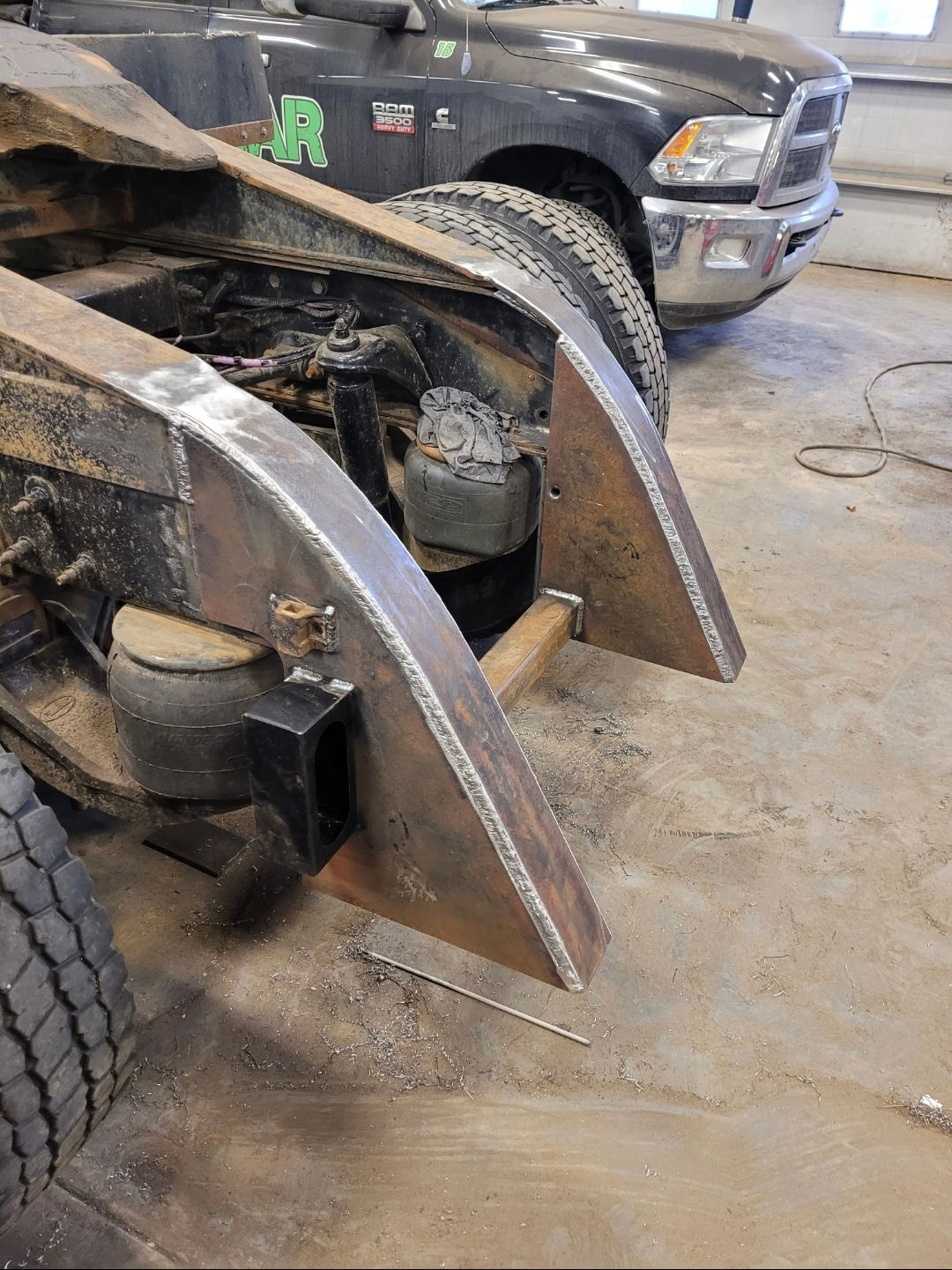 Close-up of a truck with a large metal snow plow attachment in a garage, showing muddy tires.