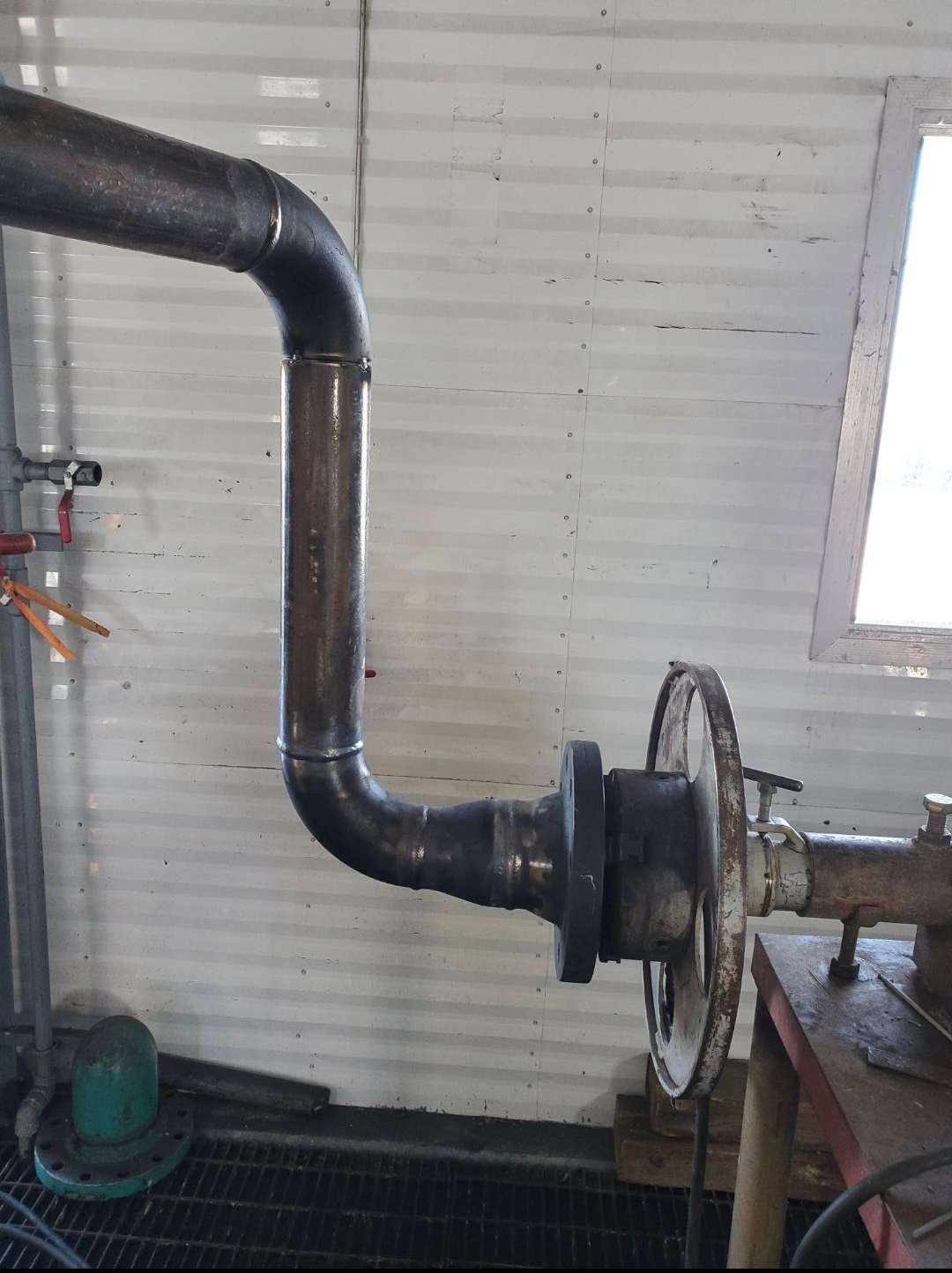 Industrial pipe with elbow joints and flange attached to machinery in a workshop.