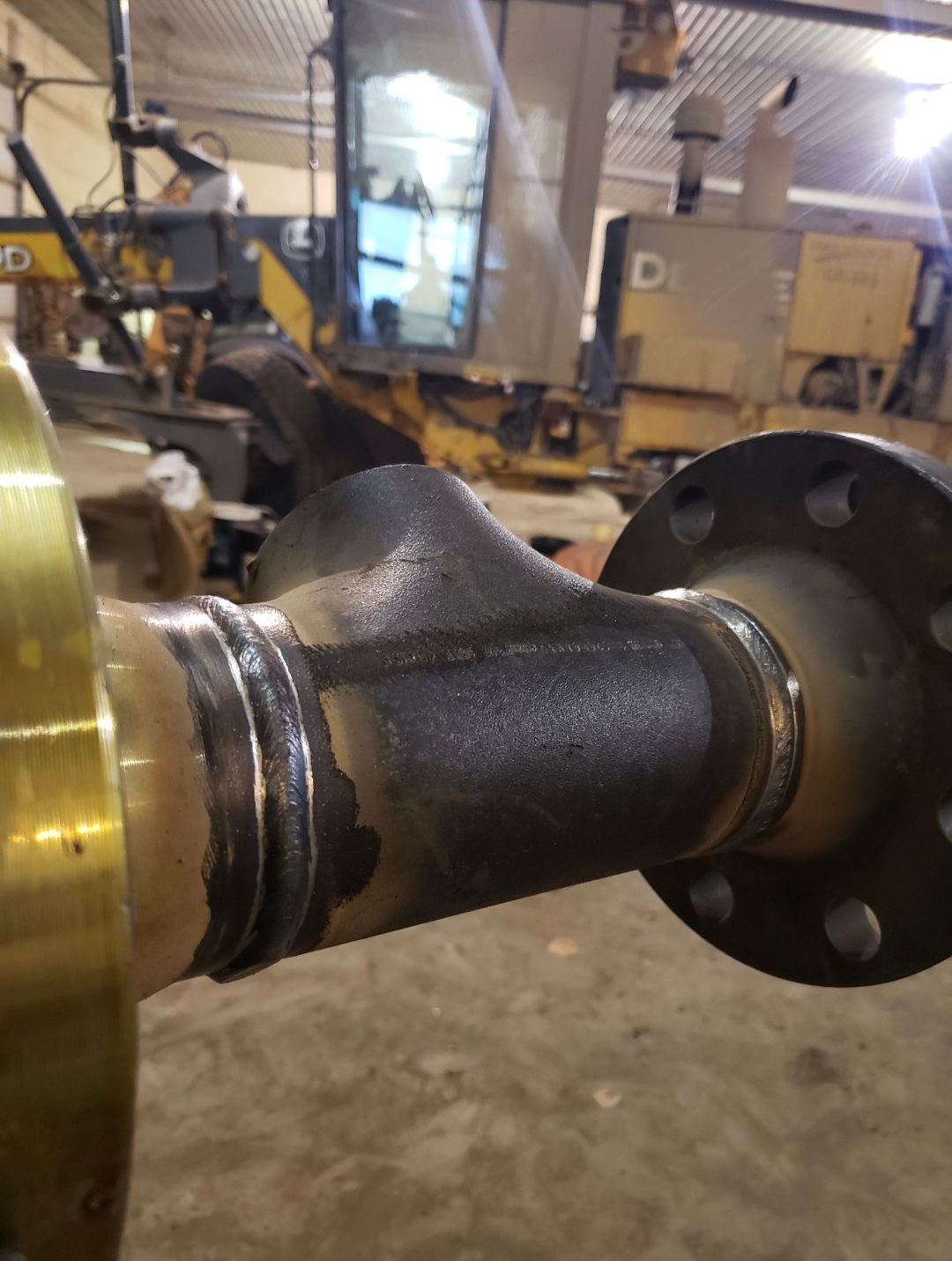 Close-up of a black metal shaft with flanges in an industrial workshop, attached to machinery.