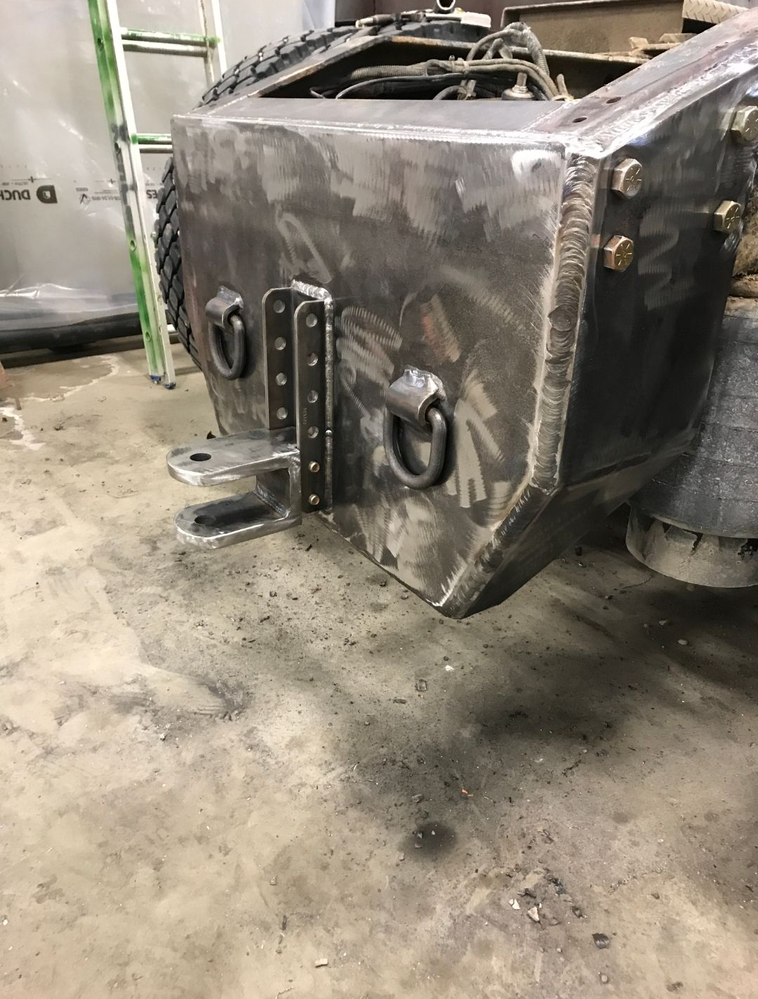 Damaged black vehicle front end with tow hitch in a dirty garage or repair shop