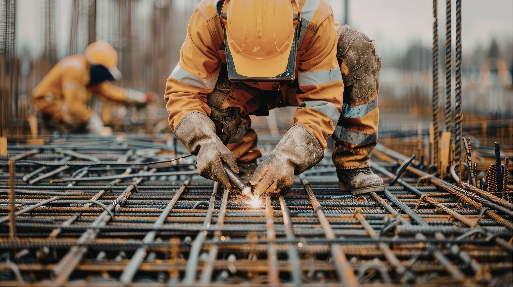 Construction worker welding steel rebar on a site, with sparks flying and another worker blurred in the background