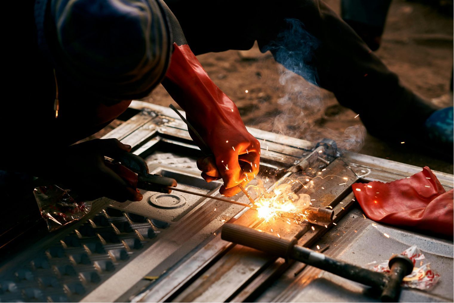 Worker welding metal with bright sparks and orange gloves on a workshop floor