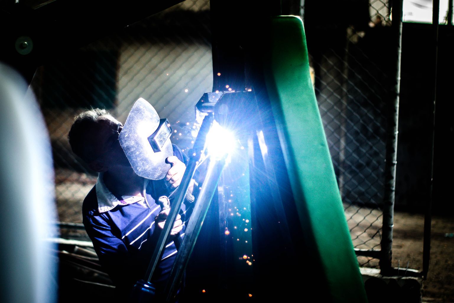 Person welding with bright blue sparks in a dark workshop