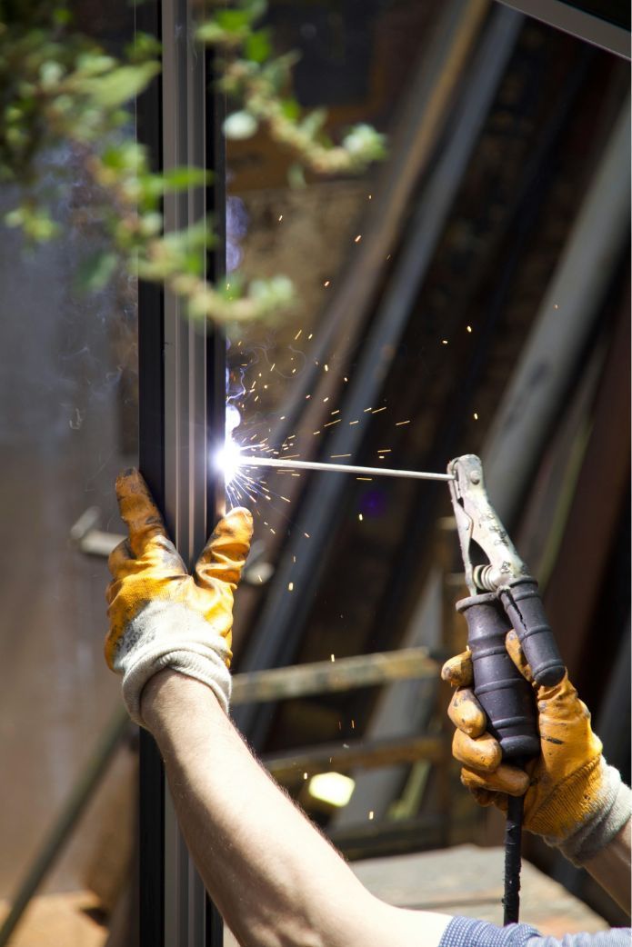 Gloved hands welding a metal frame, with bright sparks indoors.