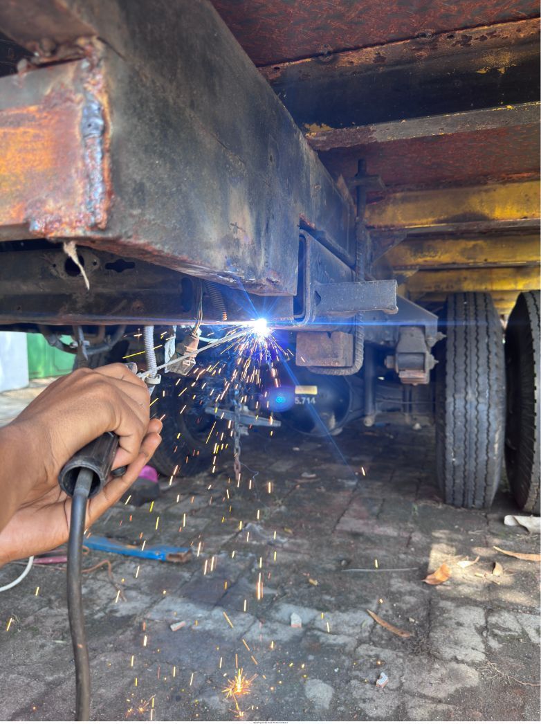 Person welding under a vehicle chassis, with bright sparks and blue arc light near a tire.