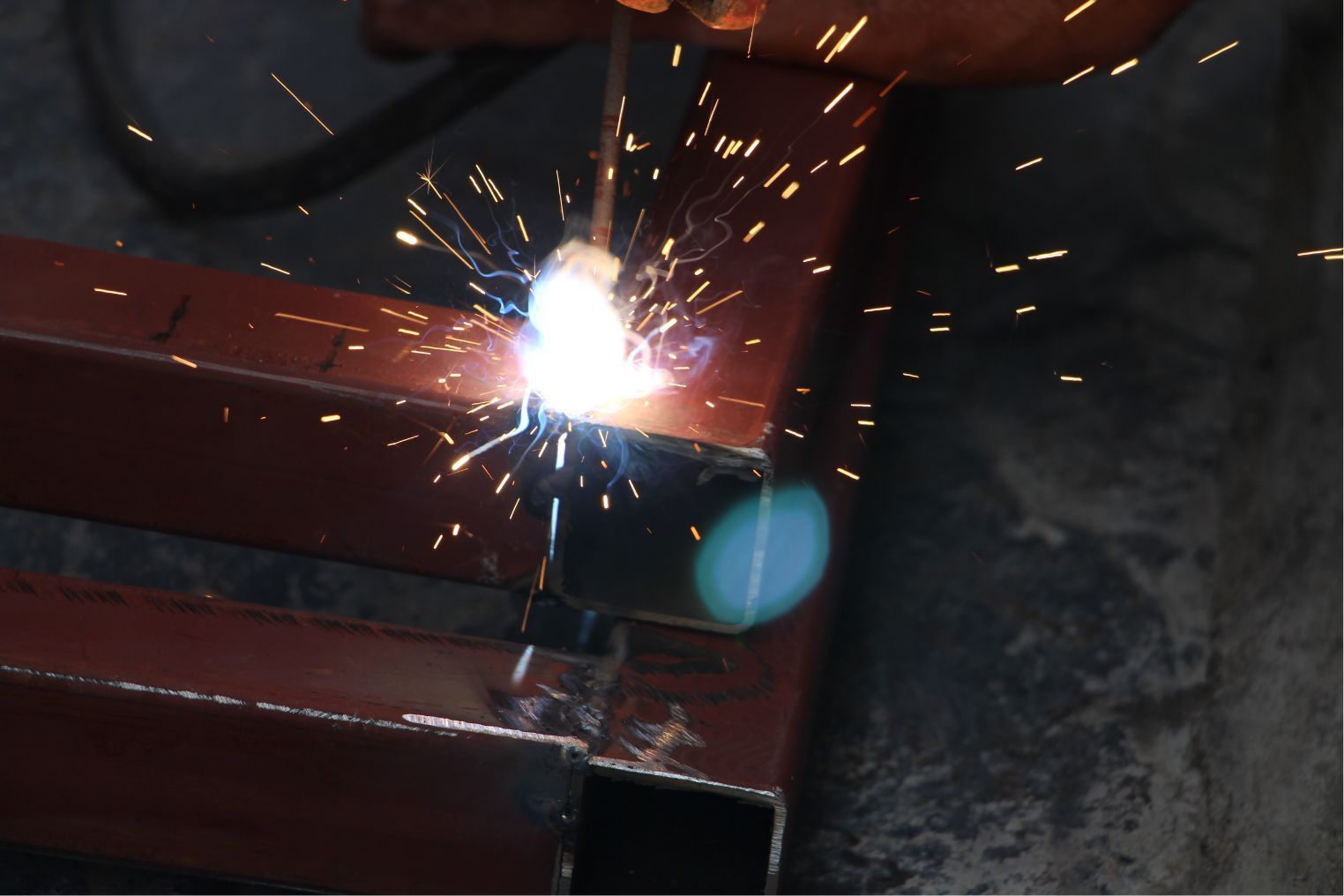 Welding sparks on a red metal structure in a dark industrial setting