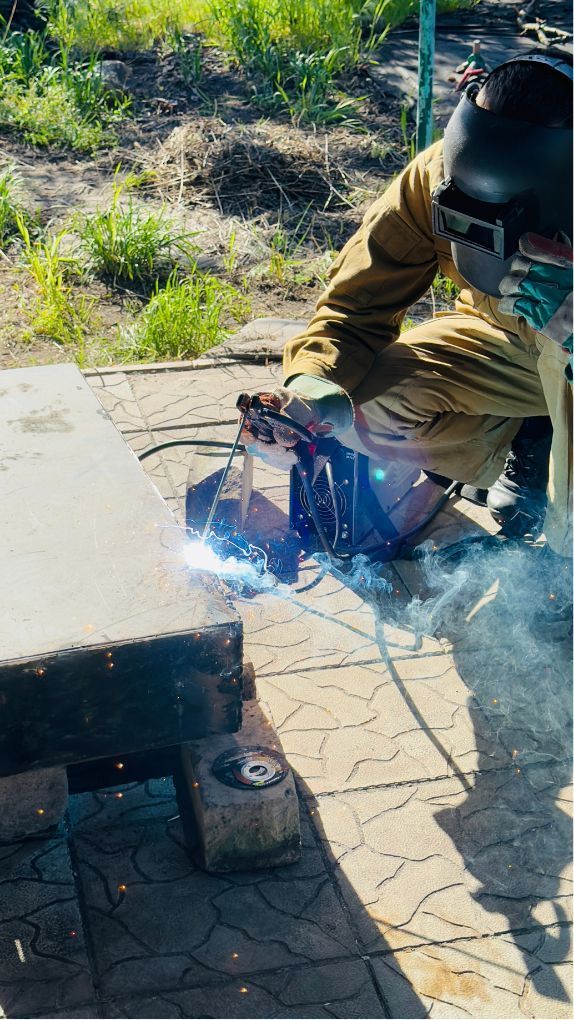 Person welding a metal piece outdoors, with bright sparks and protective gear.
