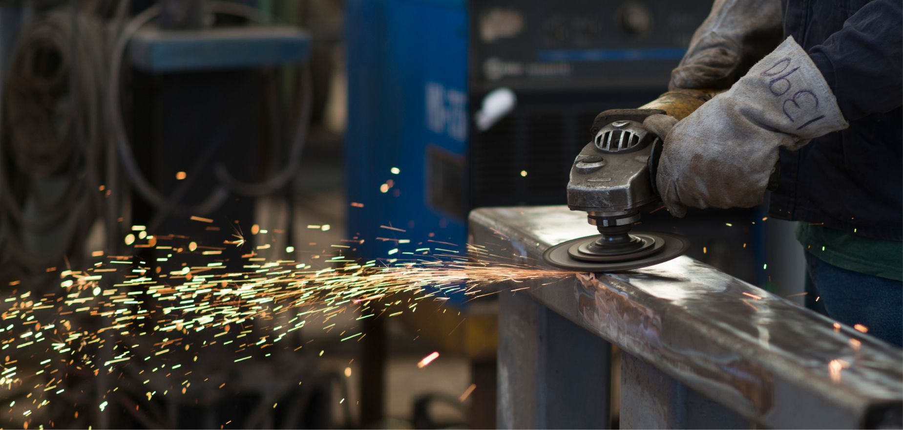 Worker using an angle grinder on metal, sending bright sparks in a workshop.
