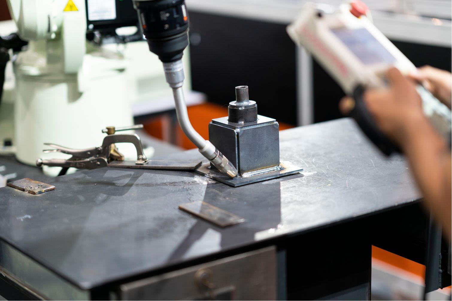 Worker using a drill press on a black metal surface in a workshop