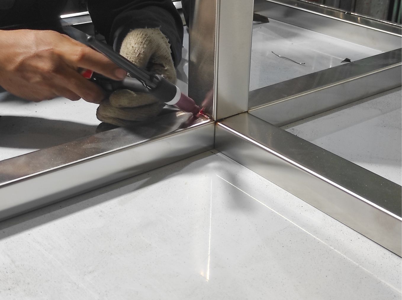 Hand using a rotary tool to smooth a metal corner seam in a stainless-steel sink frame