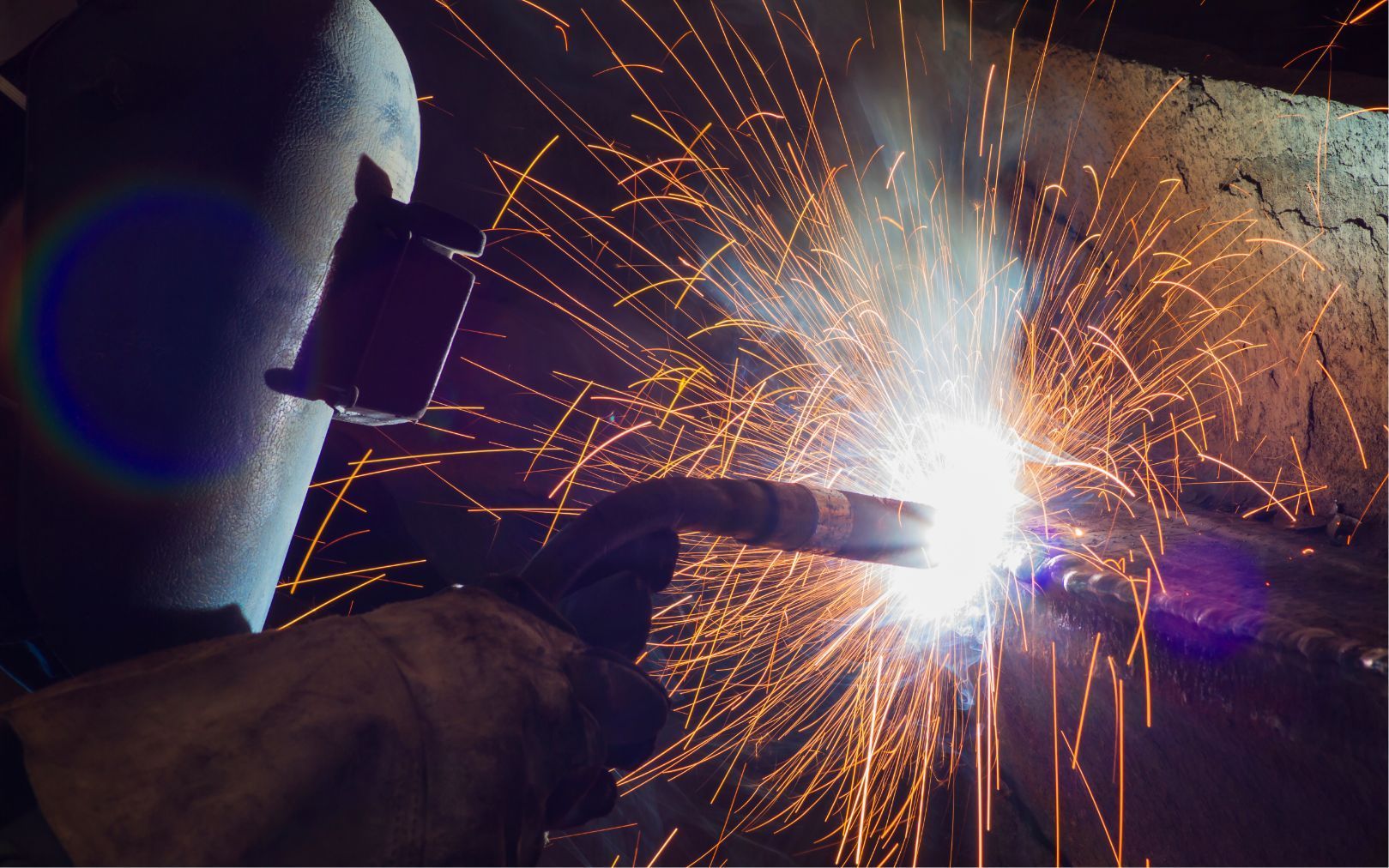 Person welding metal with bright sparks flying in a dark workshop