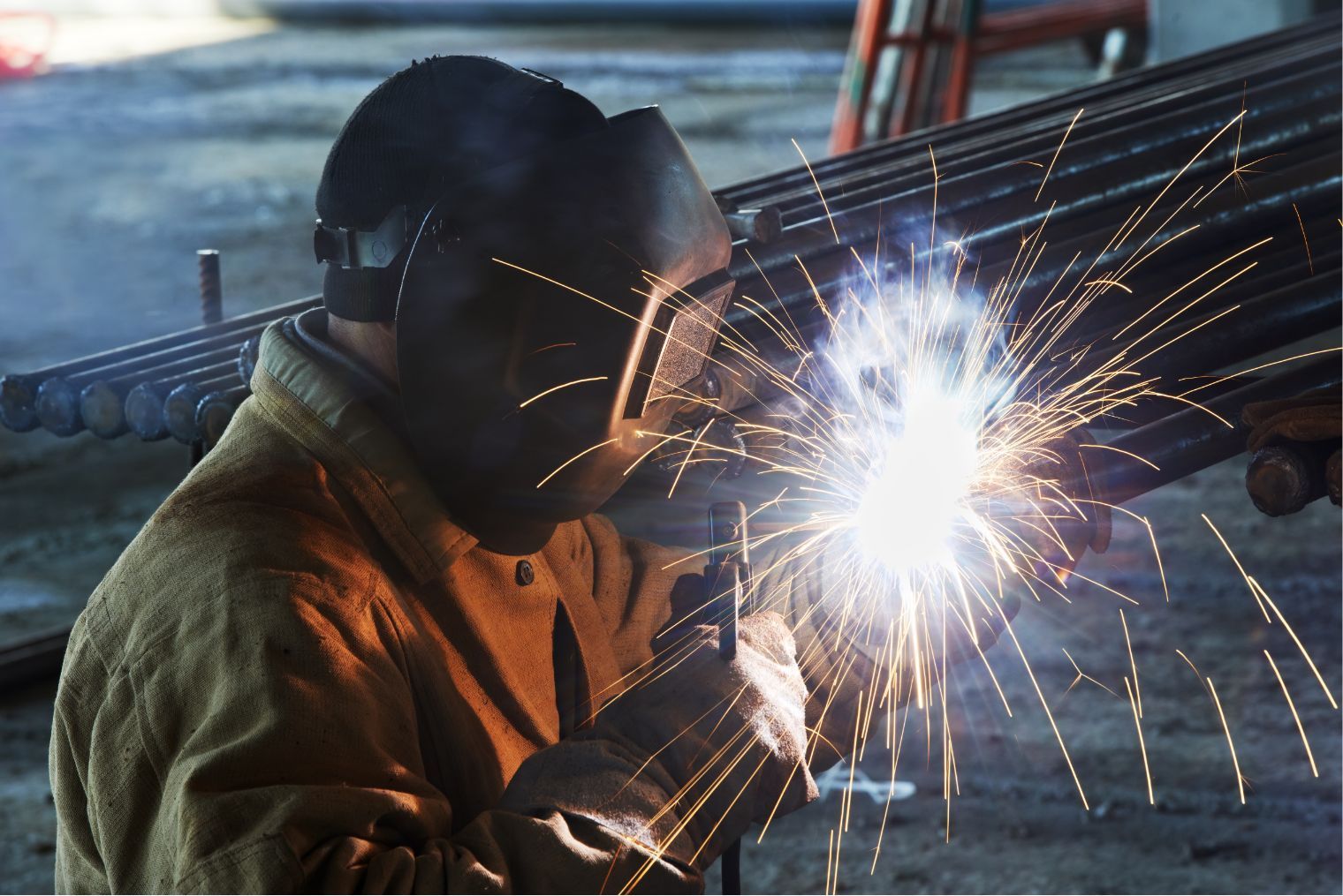 Welder in protective gear sparks metal in a workshop or outdoor industrial setting