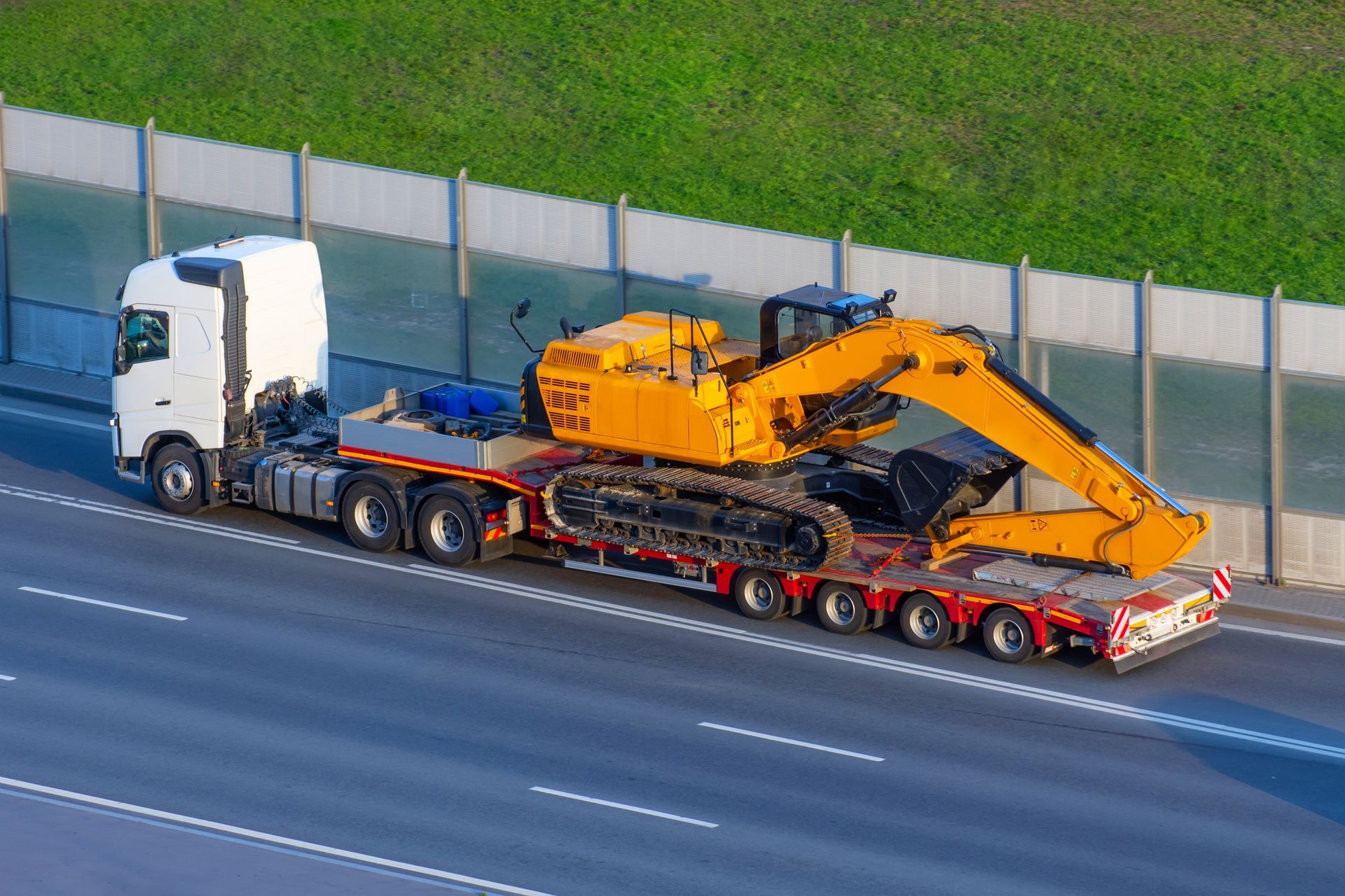 A semi truck is carrying a yellow excavator on a highway.