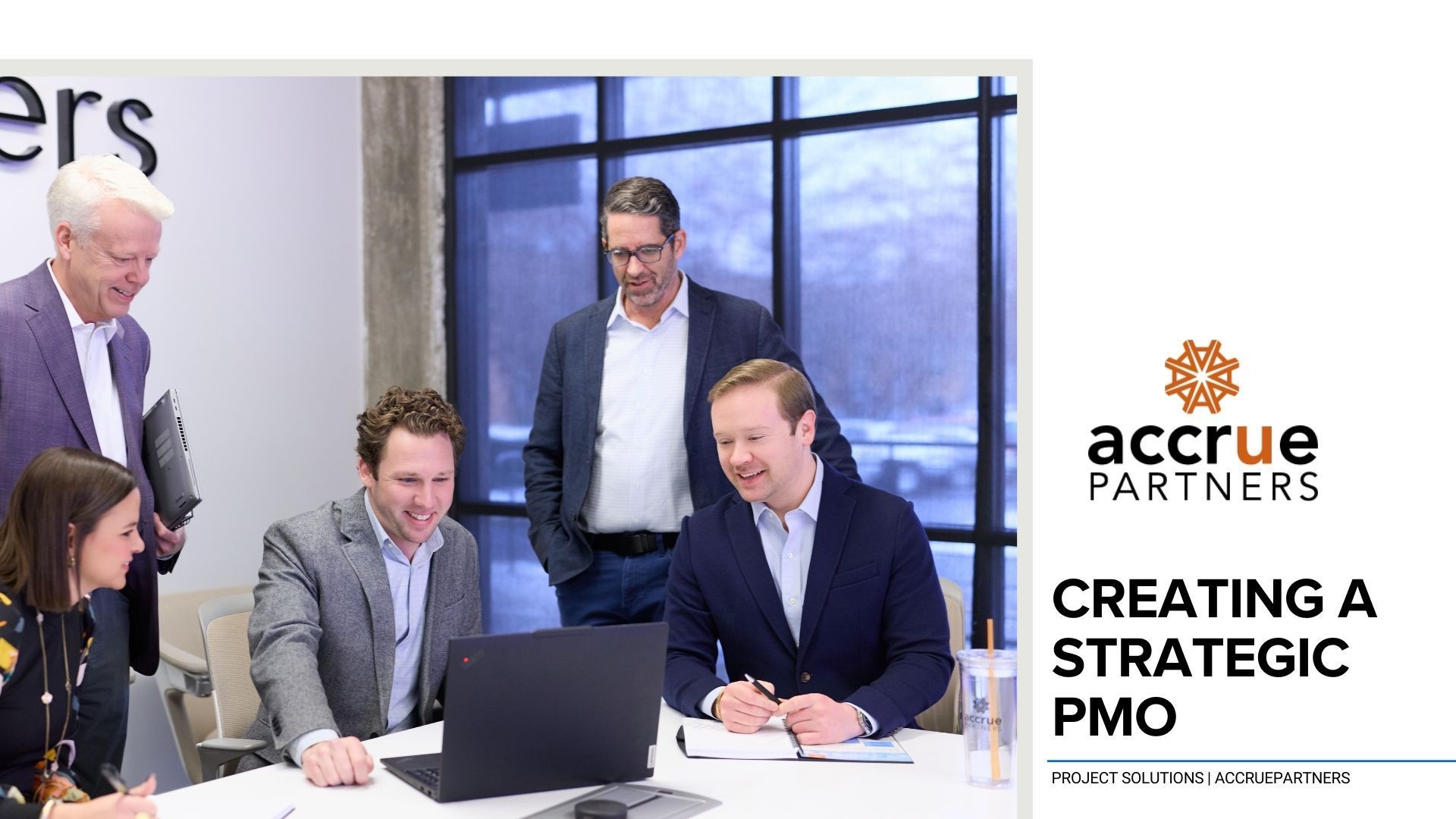 A business meeting with five people around a table looking at a laptop, with