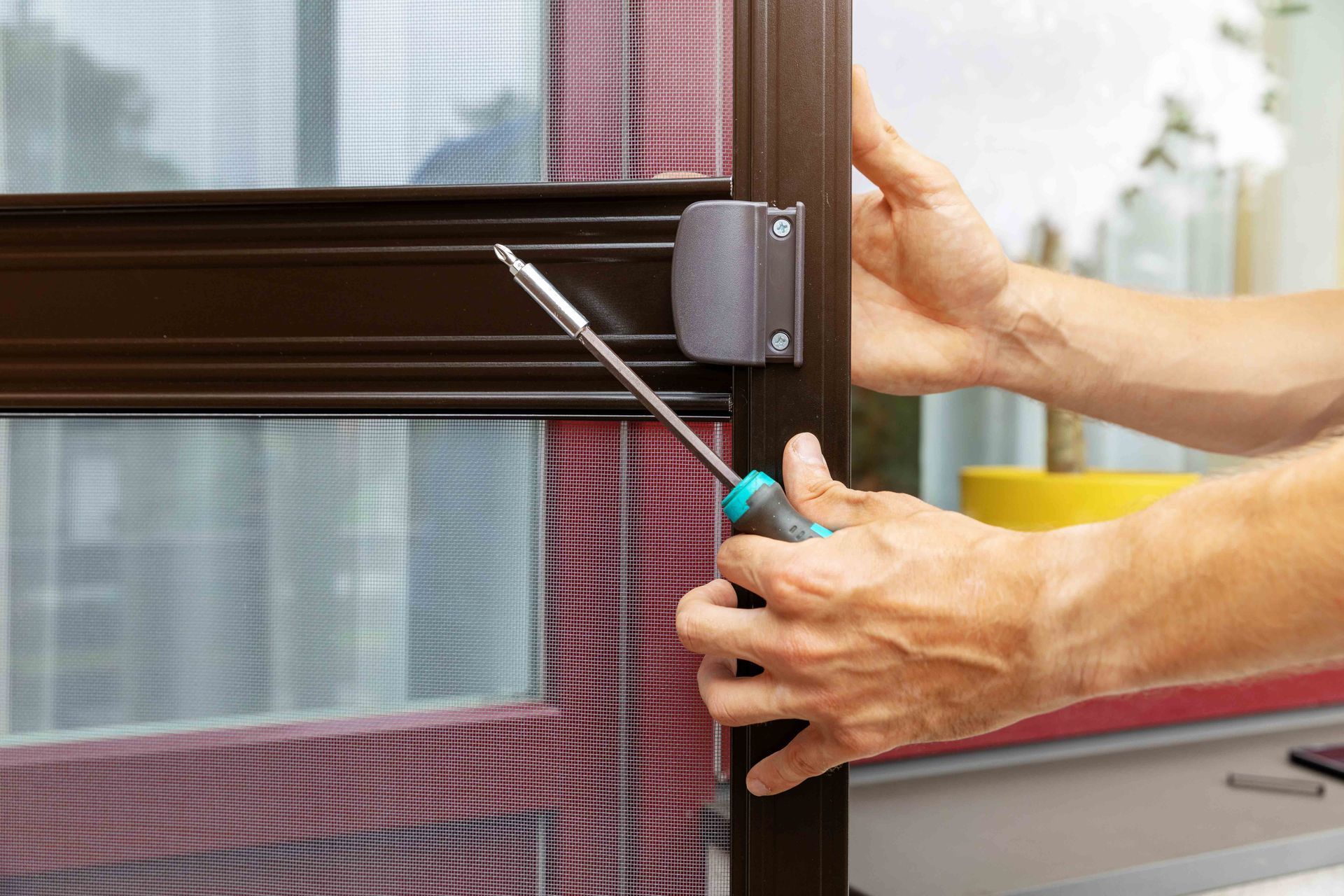 Hands using a screwdriver to install or adjust a latch on a window or sliding screen door frame.