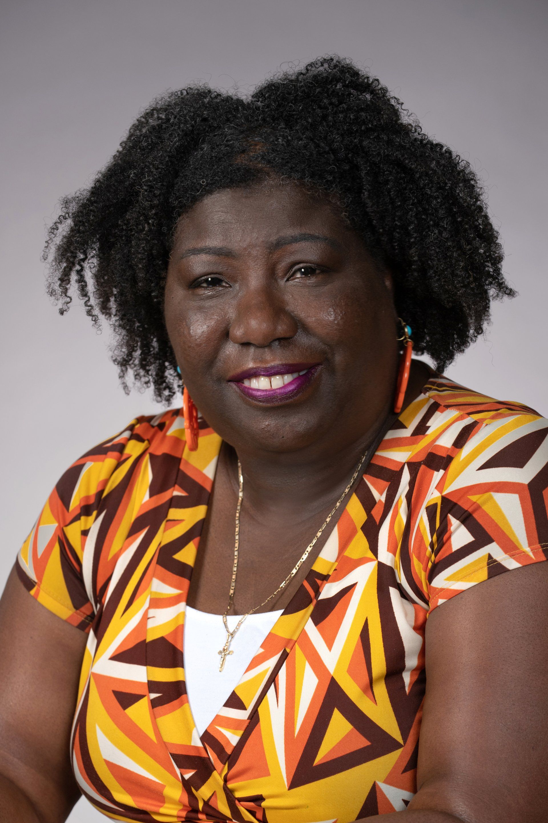 A woman wearing a colorful shirt and earrings is smiling for the camera.