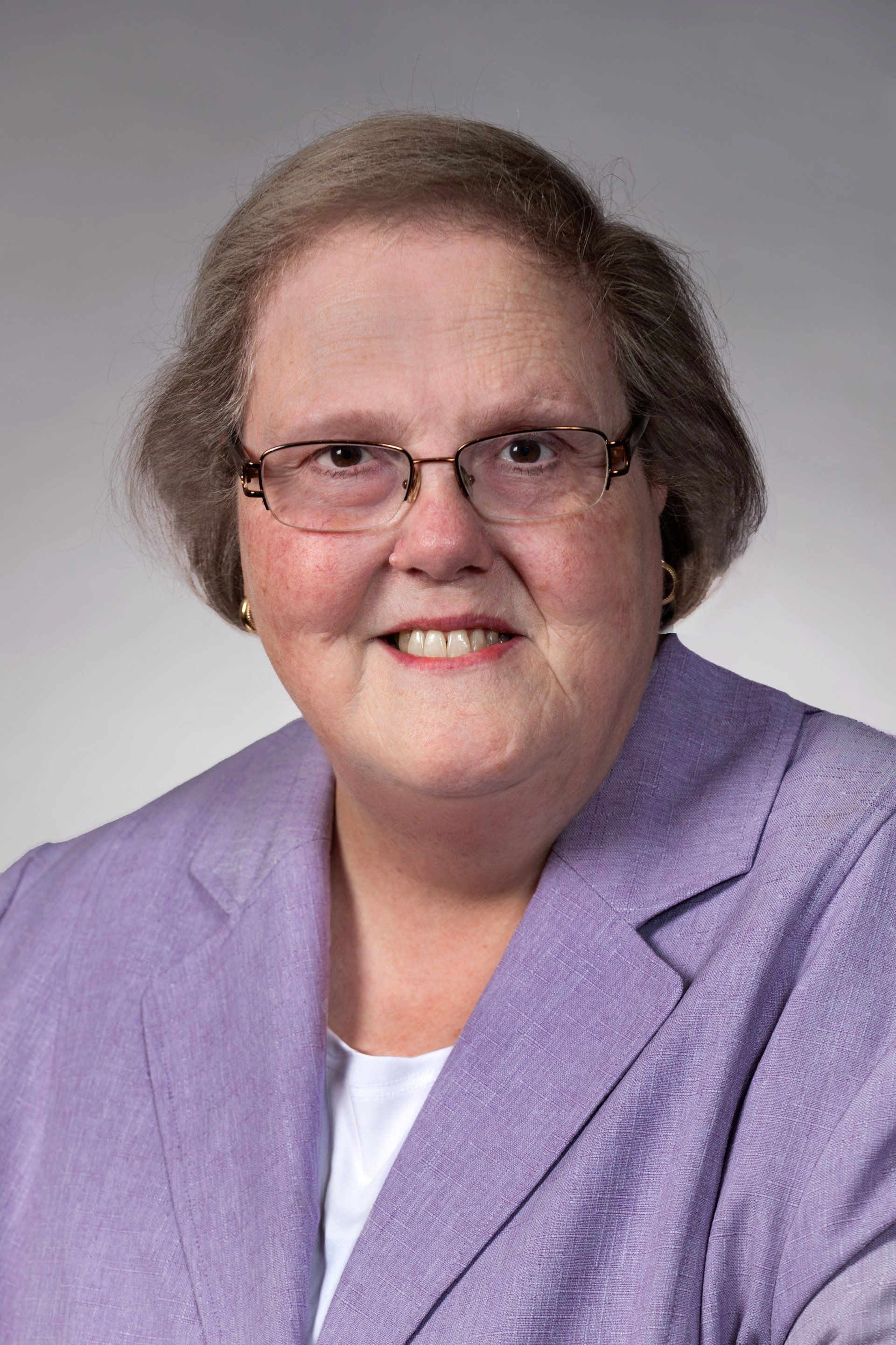 A woman wearing glasses and a purple jacket is smiling for the camera.