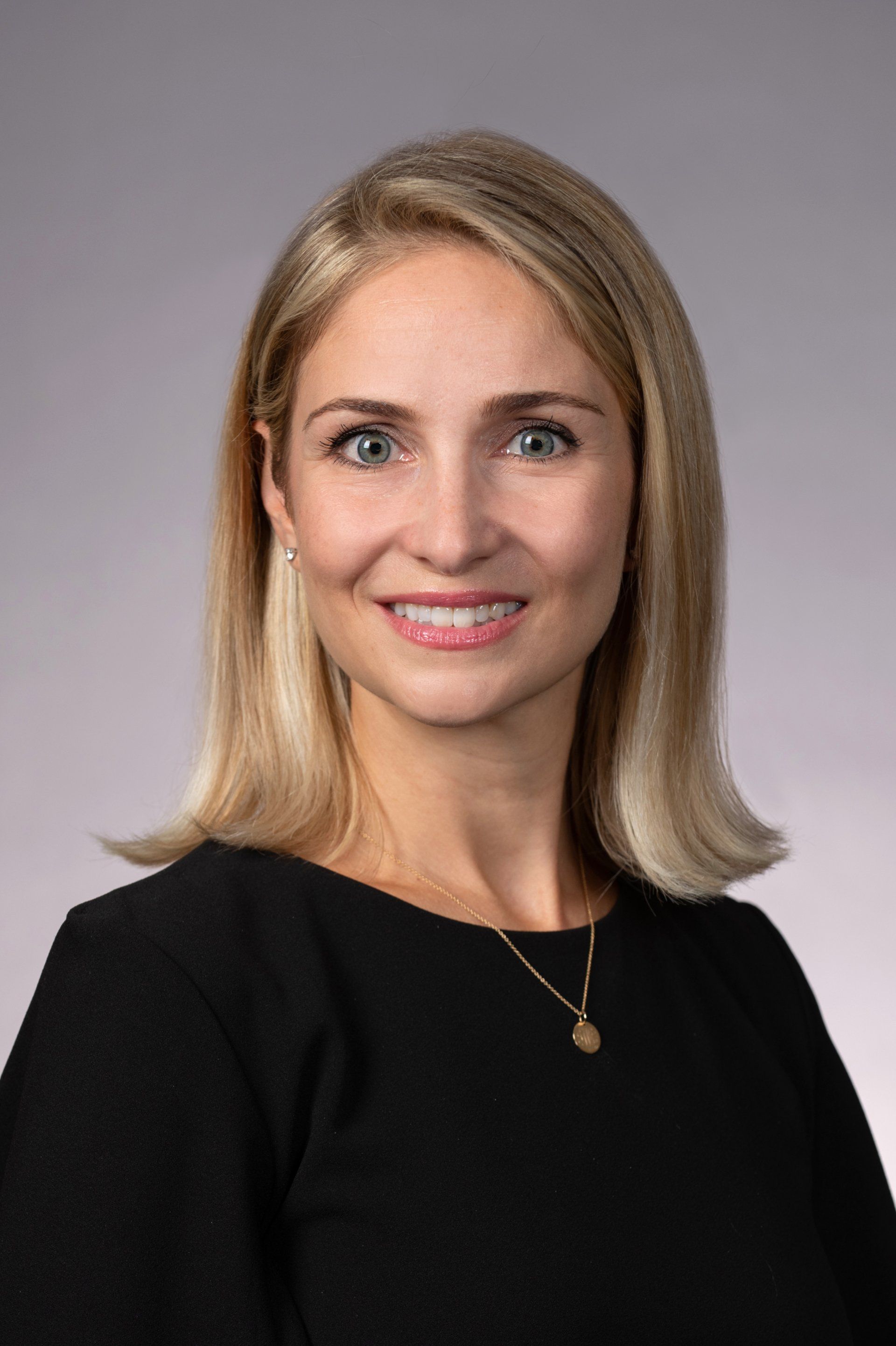 A woman in a black dress and necklace is smiling for the camera.