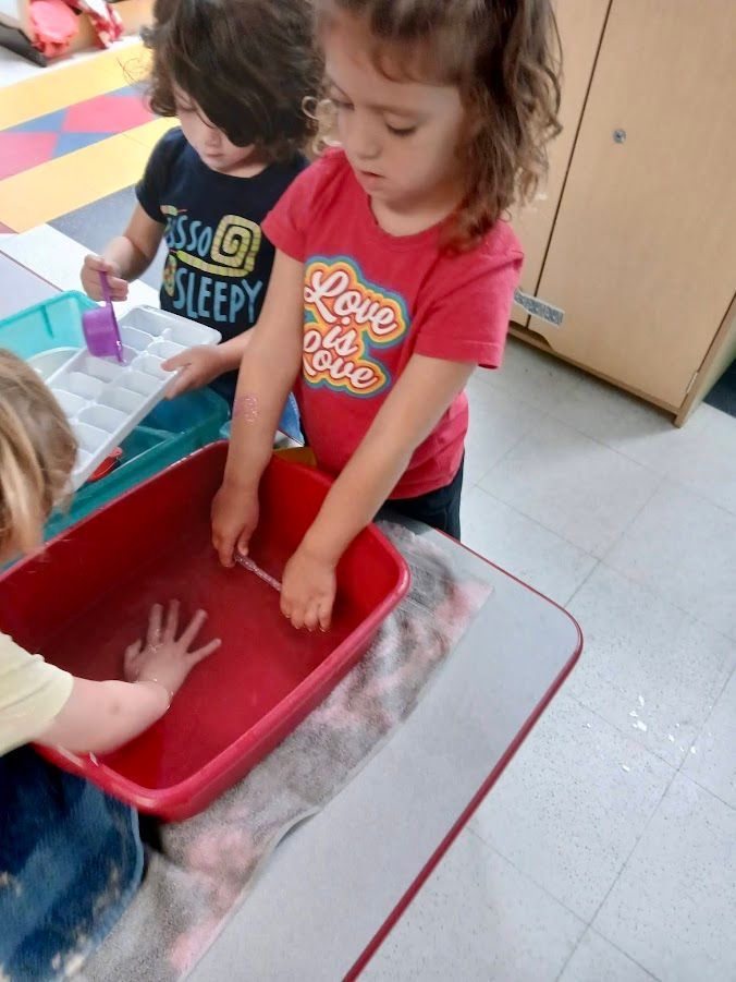 Children playing at a table with water in a red bin. 