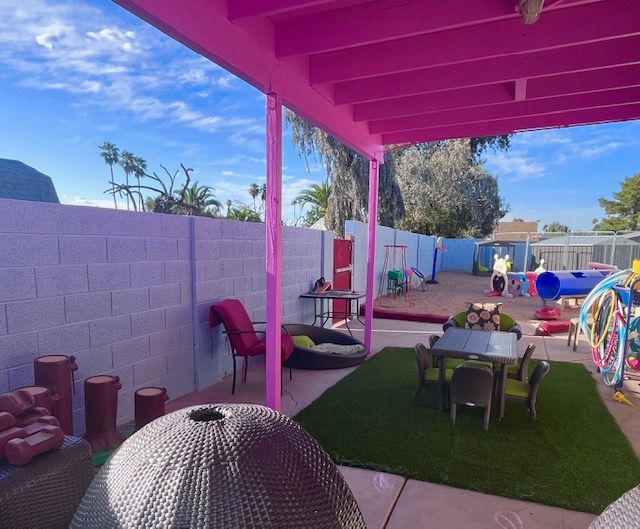 Outdoor play area with pink awning, white walls, and various toys under a blue sky.
