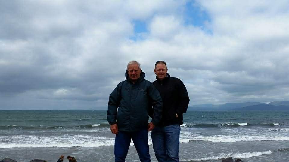 Two people standing on a windy beach under cloudy skies with choppy ocean waves