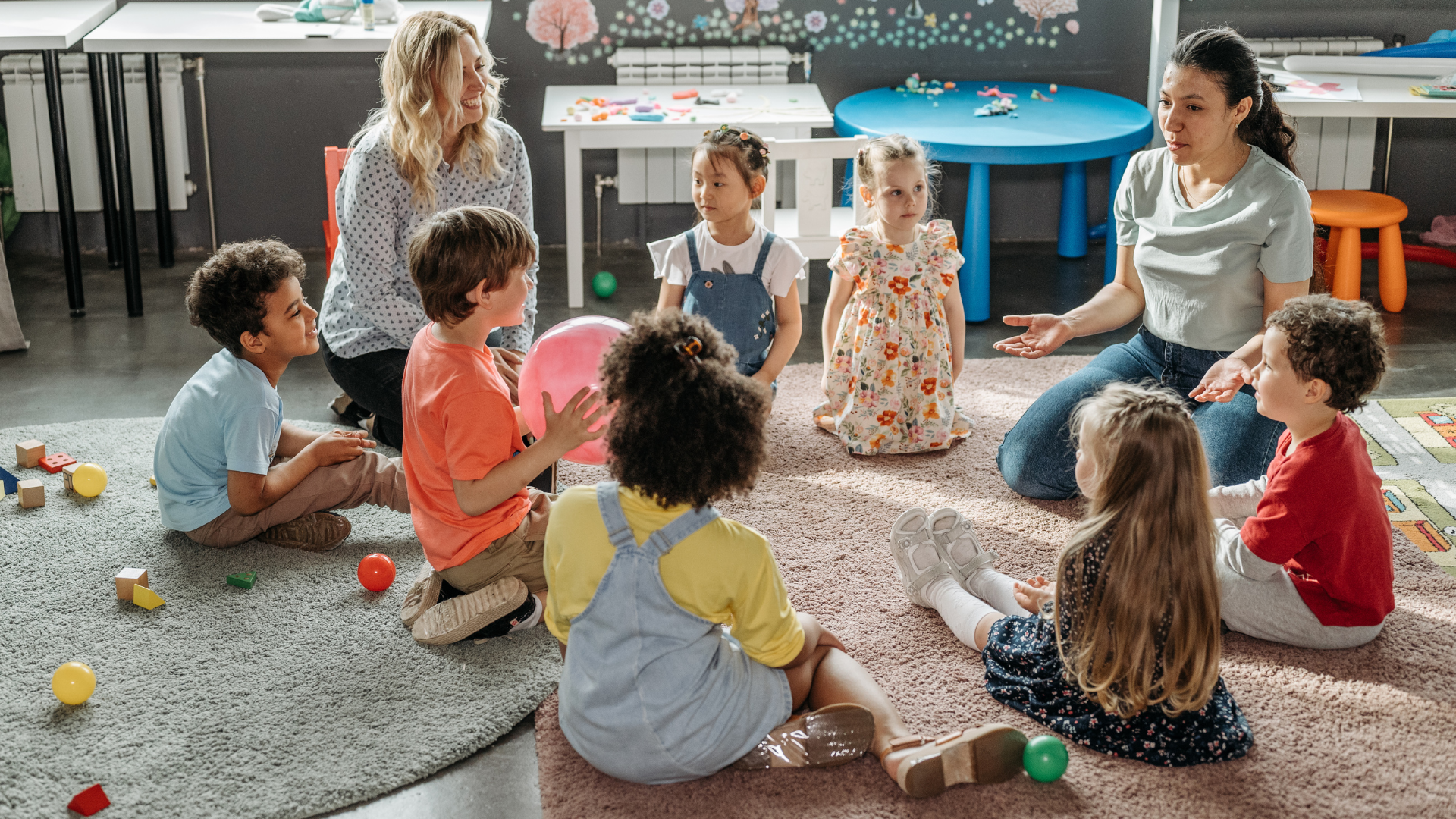 A group of children sit in a circle while playing games with two group supervisors.