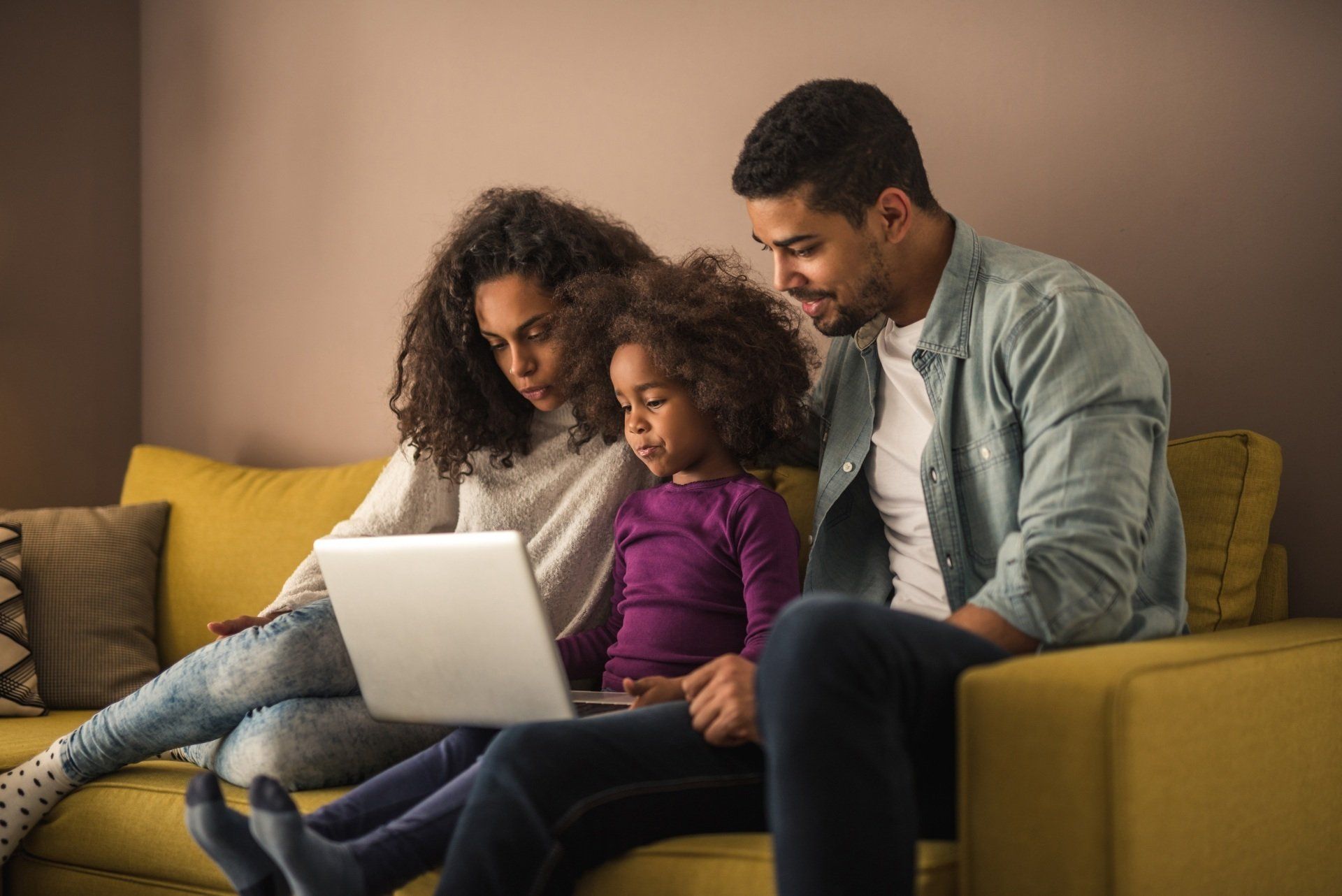 Family sitting on a couch, looking at a laptop together in a cozy living room.