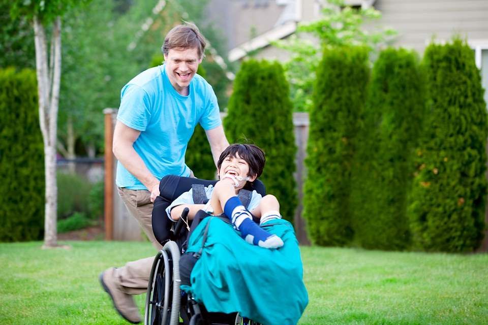 A father and his son that is in a wheelchair play in a backyard.