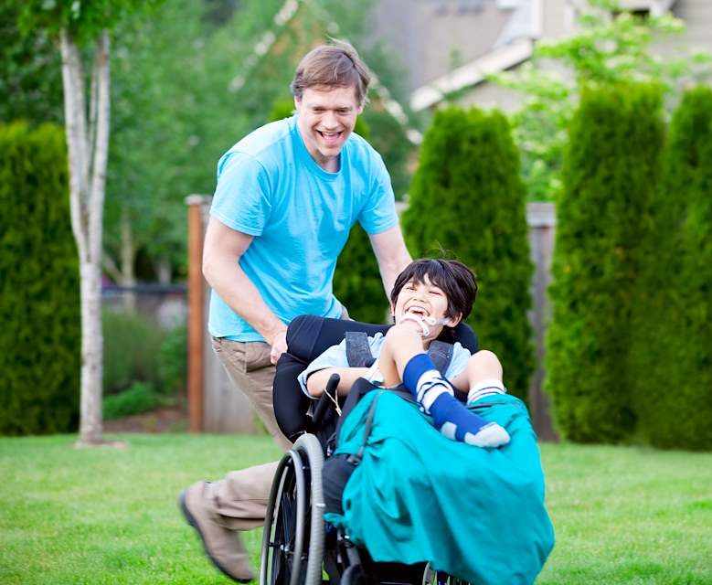 A man and child that is in a wheelchair play in a backyard.