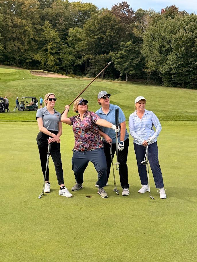 4 women make silly poses with their golf clubs while on the golf green