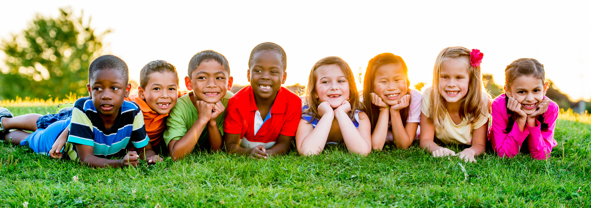 a bunch of kids in a row together on the grass smiling