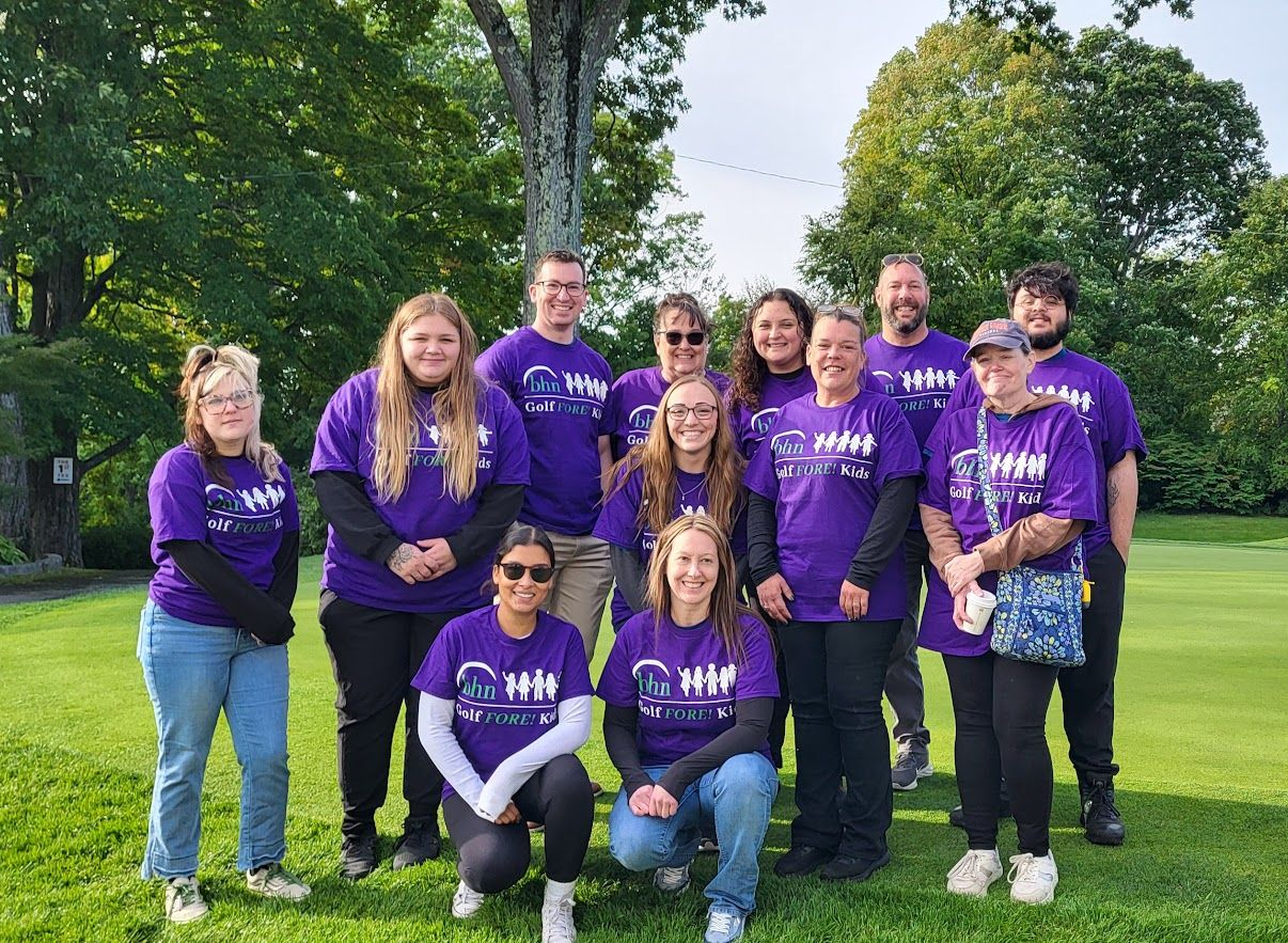 12 volunteers pose outside for a group photo while wearing their volunteer shirts