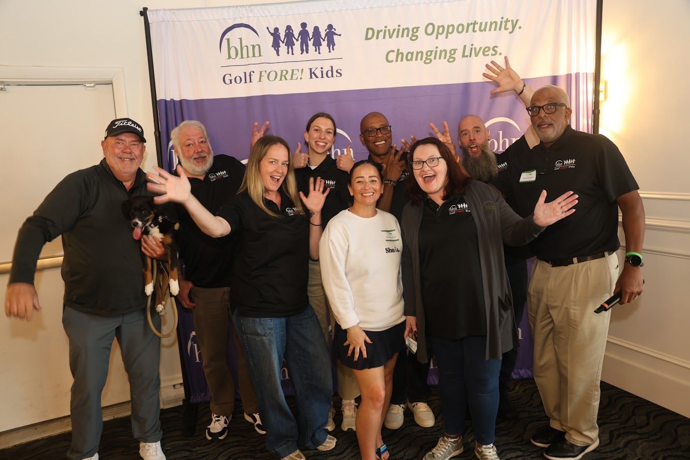 BHN's event team make silly poses for a large group photo in front of a Golf Fore! Kids backdrop.