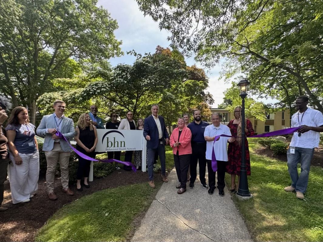 A group gathers as Rose cuts the ribbon in front of the BHN sign.