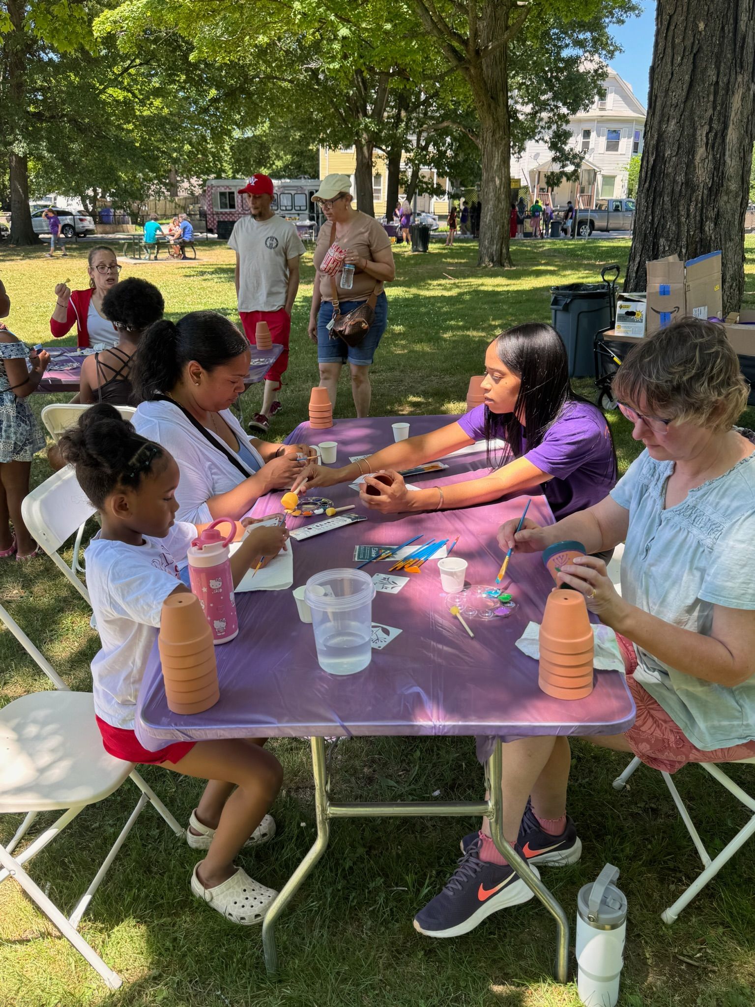 People sitting down to paint terracotta pots at a table in the park.