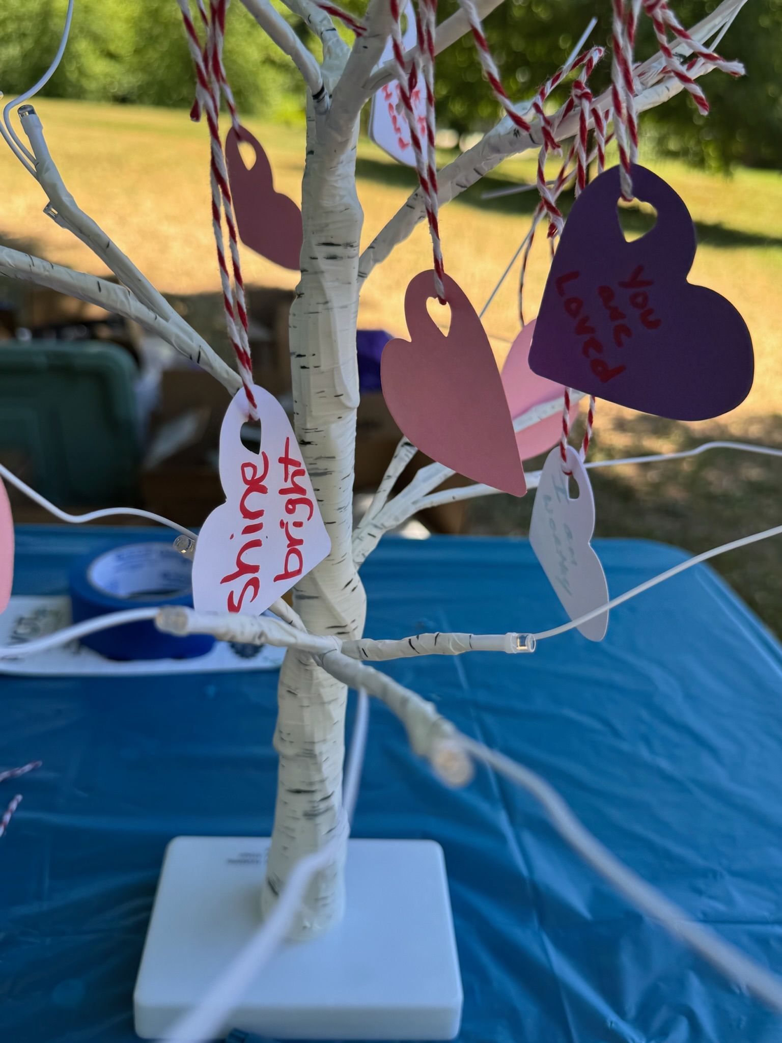 A small paper tree that's decorated with positive affirmations from event goers. The positive affirmations are on pink, purple, and white hearts that are hanging off the tree branches. They say phrases like 