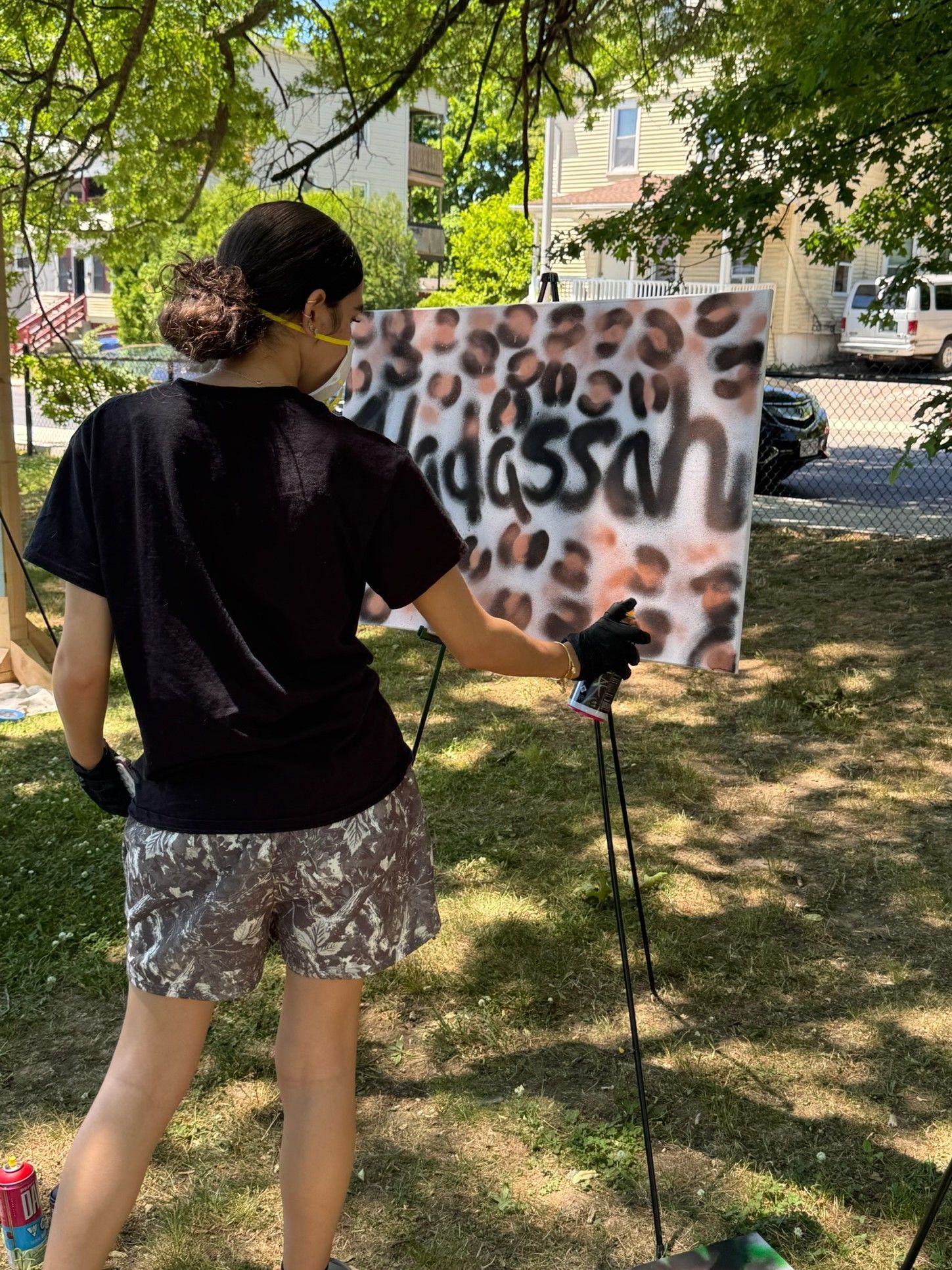 A girl spray paints her name with leopard print patterns onto a canvas in the park.