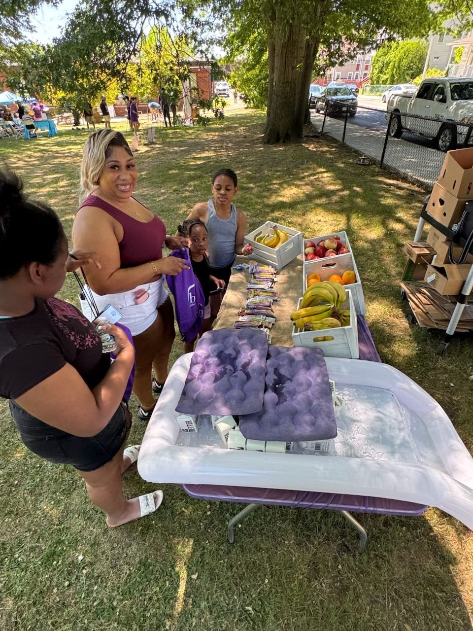 A woman and two children getting fresh fruit from a table at the park.